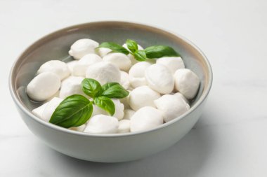 Lezzetli mozzarella peynir topları kasede ve fesleğen beyaz mermer masada, yakın plan.