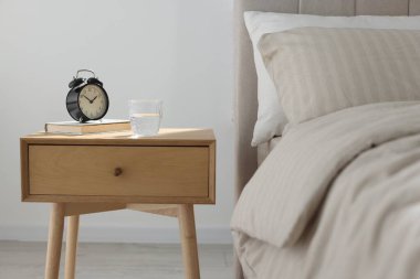 Alarmlı komodinli komodin, bir bardak su ve yatağın yanında kitap.