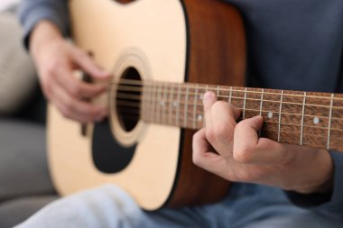 Genç adam kanepede gitar çalıyor, yakın plan.