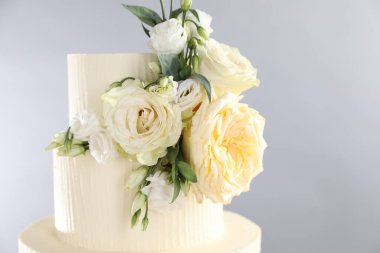 Gri arka planda çiçeklerle süslenmiş lezzetli düğün pastası, yakın plan. Metin için boşluk