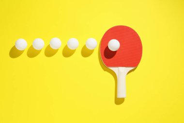 Masa tenisi raketi ve toplar sarı arka planda, düz yatıyordu