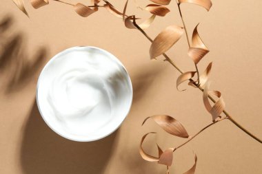 Bej arka planda bir kavanoz vücut kremi ve kuru dallar, üst manzara.