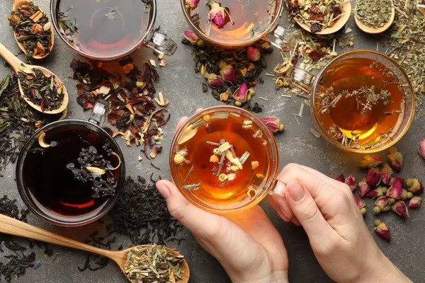 Gri masada aromatik bitki çayı, kuru yapraklar ve çiçekli bir kadın.