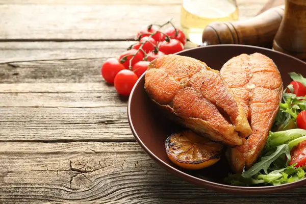 Deniz ürünleri. Tahta masada salata ve limonla servis edilen lezzetli somon biftekleri, yakın plan. Metin için boşluk