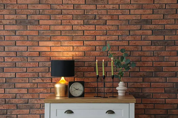 Mum ve tuğla duvarın yanındaki masada yanan mumlar.