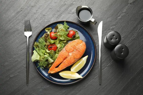 Deniz ürünleri. Siyah masada salata ve limonla servis edilen lezzetli somon bifteği.