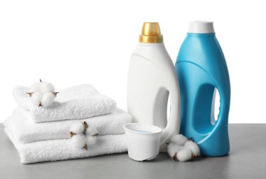 Beyaz arkaplana karşı gri masada yumuşatıcı, pamuk çiçeği ve havlu şişeleri