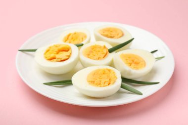 Pembe arka planda haşlanmış yumurta ve yeşil soğan, yakın plan.