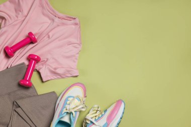 Spor kıyafetleri, spor ayakkabıları ve soluk zeytin arka planda dambıllar, düz yatış. Metin için boşluk