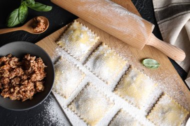 Pişmemiş ravioli, merdane, bolonez ve fesleğen siyah masada, düz yatıyordu.