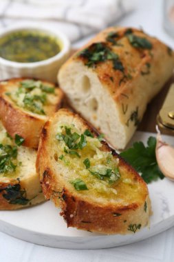 Sarımsaklı lezzetli ekmek, otlar ve yağlı beyaz fayanslı masa, yakın çekim.