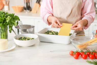 İçerideki mermer masada ıspanaklı lazanya yapan kadın, yakın plan.