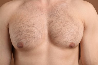 Kıllı göğüslü, kahverengi arka planda genç bir adam, yakın plan. Epilasyon işlemi