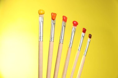 Sarı arkaplanda renk boyalı birçok fırça, yakın plan