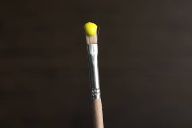 Ahşap arka planda sarı boyalı fırça, yakın plan.