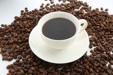 Fincanda Aromatik kahve ve beyaz arka planda fasulye, yakın plan.