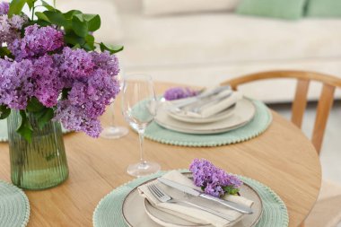 Güzel leylak çiçekleri, tabaklar, çatal bıçak takımı ve bardaklar kapalı bir masada.