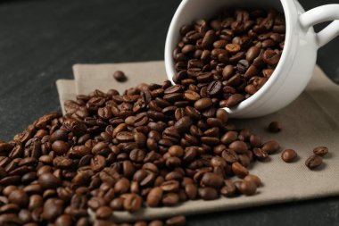 Aromatik kahve çekirdekleri ve siyah masada ters çevrilmiş fincanlar, yakın plan.