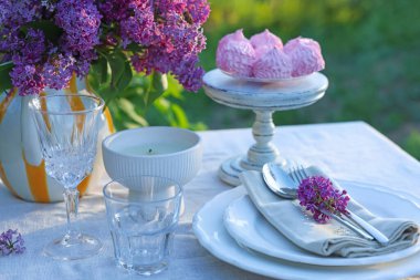 Güzel leylak çiçekleri, zephyrler, tabaklar, çatal bıçak takımı, bardaklar ve mum bahçede, yakın plan