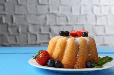 Açık mavi ahşap masa üzerinde pudra şekeri ve böğürtlenli Lezzetli kek, yakın plan. Metin için boşluk