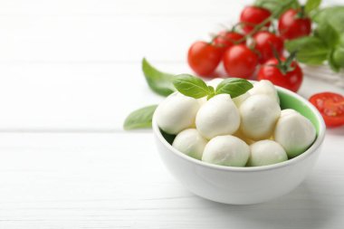 Lezzetli mozzarella peynir topları kasede fesleğen ve domatesler beyaz ahşap masada, yakın plan. Metin için boşluk