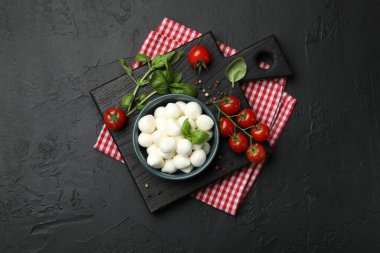 Lezzetli mozzarella peynir topları kasede, fesleğende, biberlikte ve domateslerde siyah masada, üst tarafta.