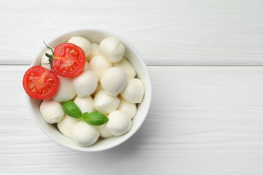 Lezzetli mozzarella peynir topları kasede, fesleğen ve domates beyaz ahşap masada, üst manzara. Metin için boşluk