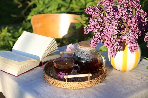 Bahçedeki masada güzel leylak çiçekleri, çay ve kitap.