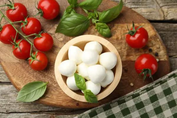 Lezzetli mozzarella peynir topları kasede, fesleğende, biberlikte ve domateslerde ahşap masada, üst tarafta.