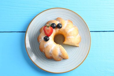 Açık mavi ahşap masada pudra şekeri ve böğürtlenli lezzetli kek.