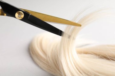 Açık gri arka planda makasla sarı saç tokası kesiliyor. Yakın plan.