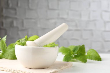 Taze limon merhemi yaprakları ve beyaz ahşap masa üzerinde havan topuzu.