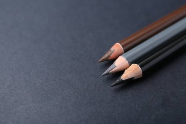 Koyu arka planda üç farklı kaş kalemi, yakın plan. Metin için boşluk