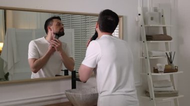 Yakışıklı adam banyoda aynanın yanında tıraş makinesiyle tıraş oluyor.