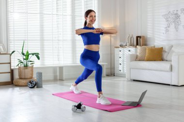 Evde dizüstü bilgisayar başında egzersiz yapan mutlu bir kadın.