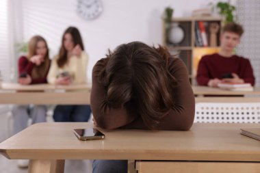 Siber zorbalık. Akıllı telefonlu ve sınıf arkadaşları tarafından sınıfa gösterilen, seçici odaklı üzgün bir genç kız.