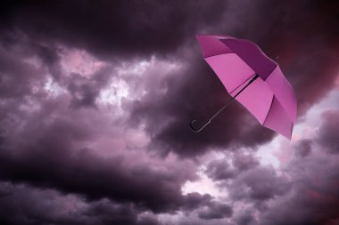 Pembe şemsiye kara bulutlu gökyüzünde uçuyor. Fırtınalı hava