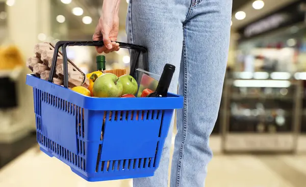 Süpermarkette elinde farklı gıda ürünleri olan alışveriş sepeti tutan kadın.