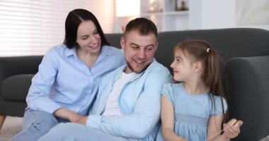 Mutlu ebeveynler ve kızları evdeki kanepede birlikte oturuyorlar.