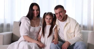Mutlu ebeveynler ve kızları evdeki kanepede birlikte oturuyorlar.