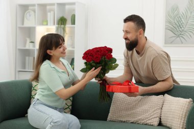 Evdeki sevgilisine kırmızı gül buketi ve hediye kutusu sunan bir adam.