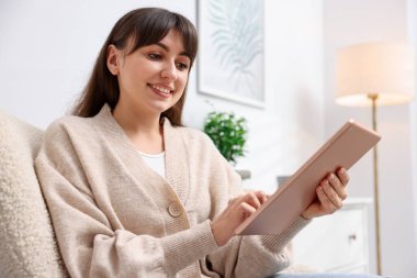 Evdeki koltukta modern tablet kullanan bir kadın. Metin için boşluk