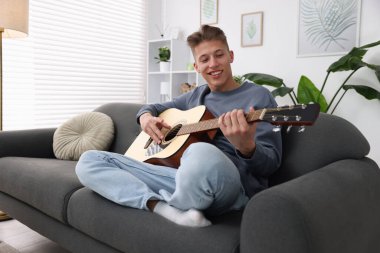 Mutlu adam içeride kanepede gitar çalıyor.
