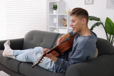 Mutlu adam içeride kanepede gitar çalıyor.