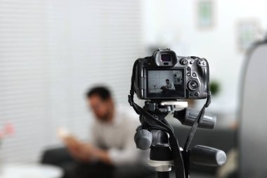 Stüdyoda koltukta oturan adam, onu kaydeden kameraya odaklan.