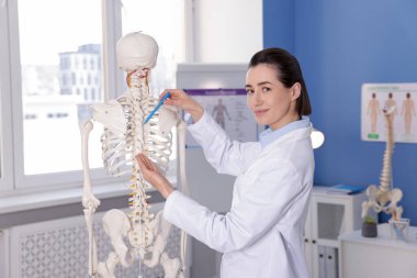 Doktor klinikteki insan iskeleti modelini işaret ediyor.