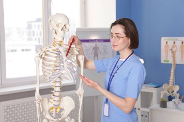 Doktor klinikteki insan iskeleti modelini işaret ediyor.