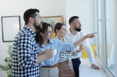 Ofisteki kahve molasında pencereden bakan meslektaşlar.