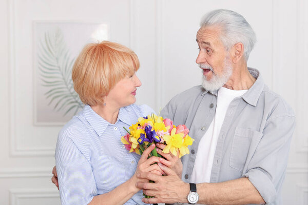 Lovely senior couple with bouquet of flowers at home