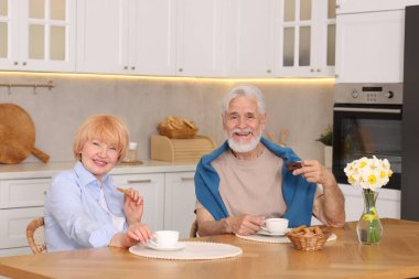 Mutfaktaki ahşap masada birlikte kahvaltı eden sevimli yaşlı çift.